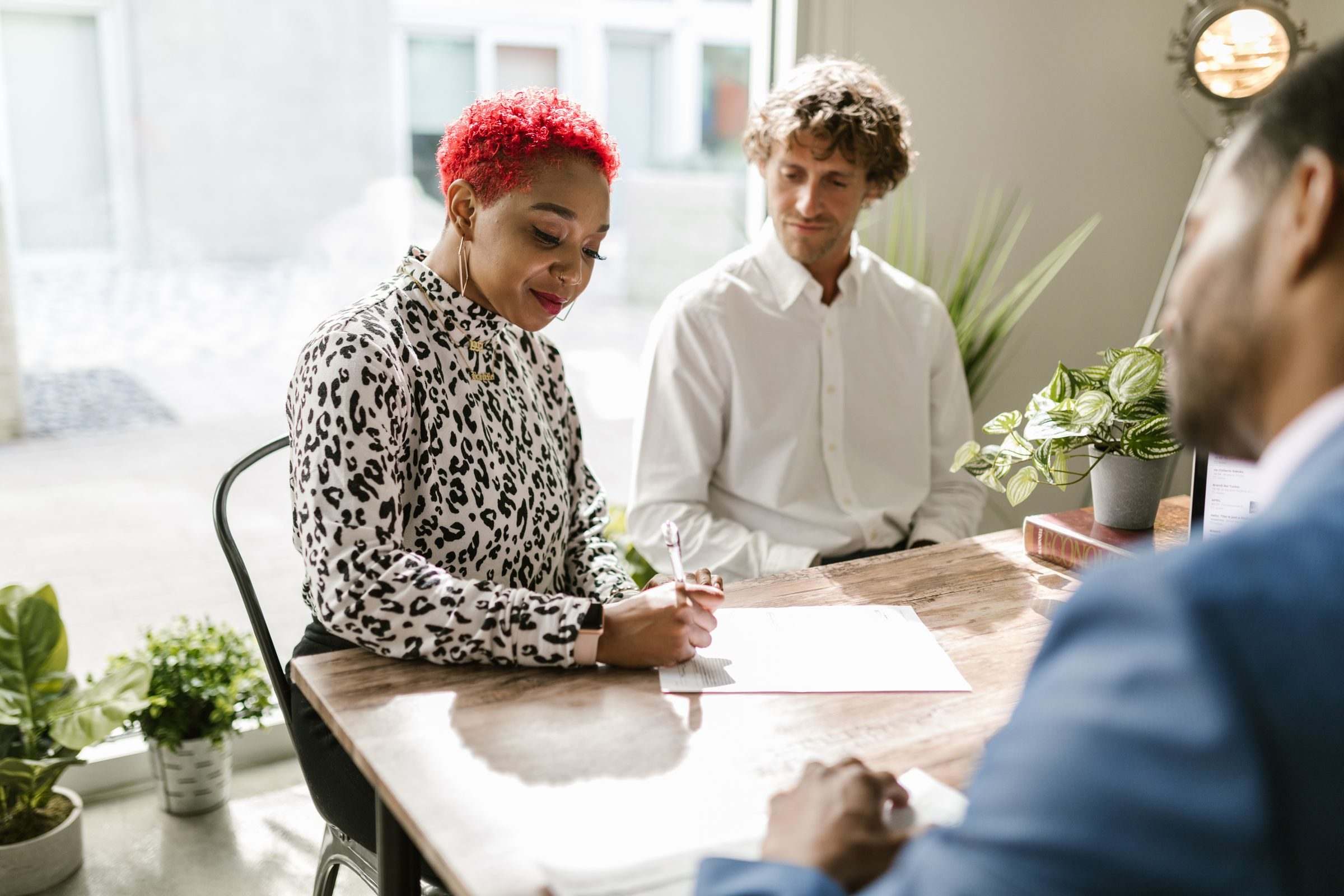 Relaxed meeting at a wooden table with plants, three people reviewing papers together